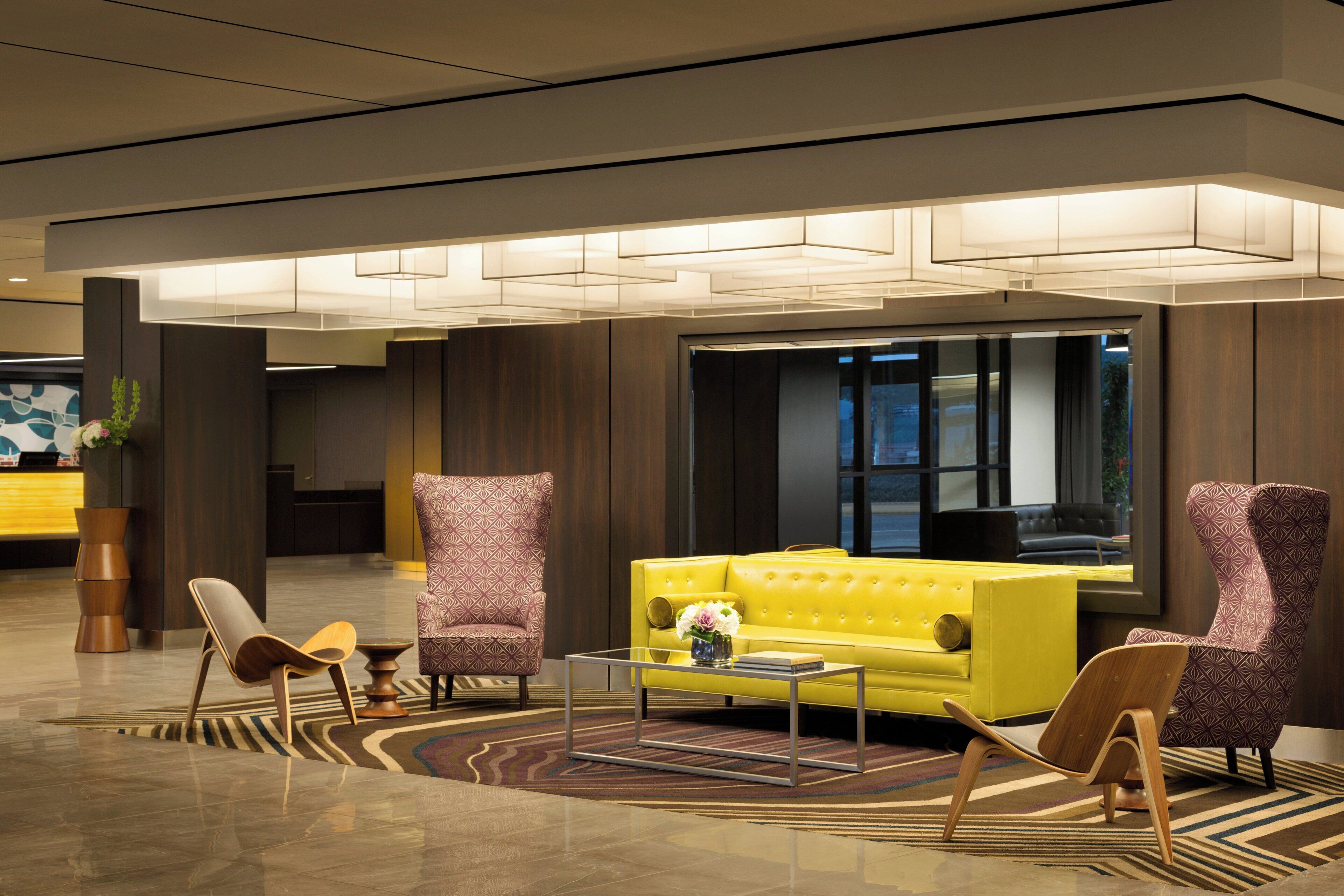 Un vestíbulo moderno con un sofá amarillo, sillones estampados, una mesa de centro y un jarrón decorativo.