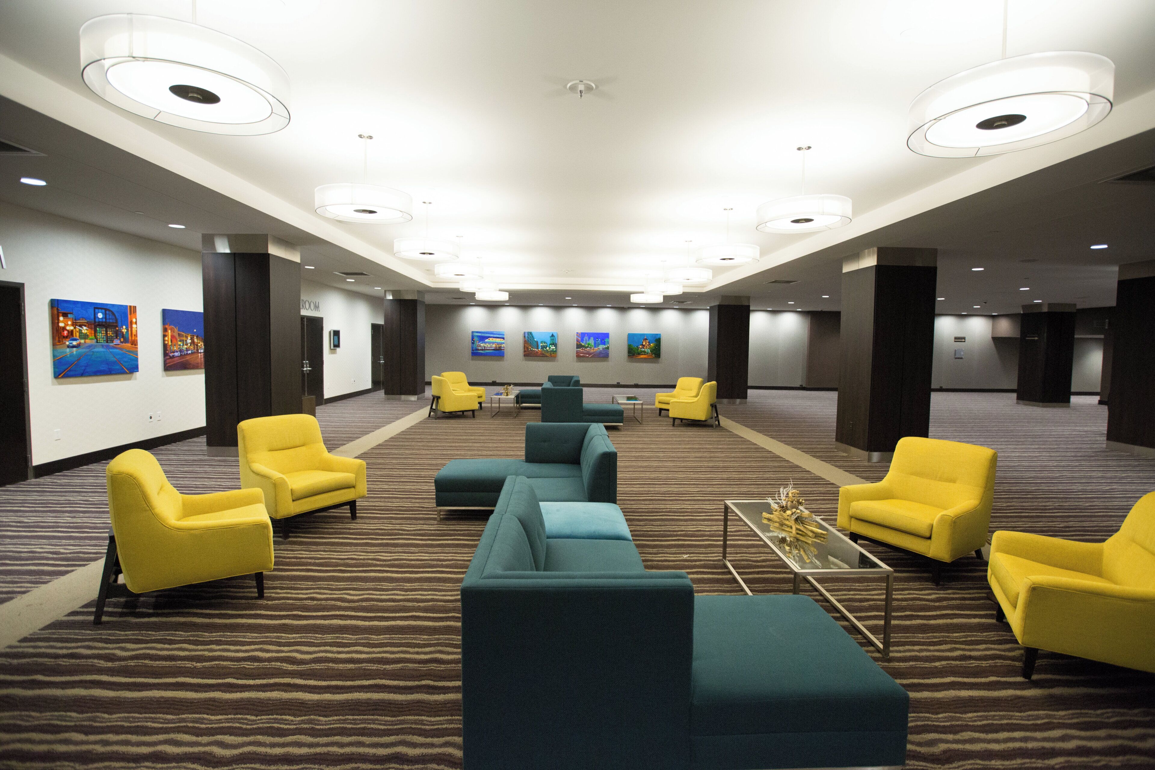 A hotel lobby with multiple seating areas, a patterned carpet, and artwork on the walls.