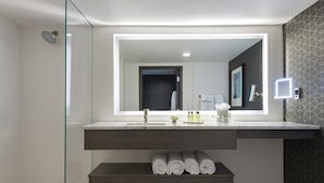 Un baño moderno con cabina de ducha de vidrio, un espejo grande y un estante empotrado con toallas dobladas.