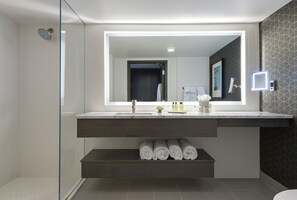 Een moderne badkamer met een douchecabine van glas, een grote spiegel en een inbouwkastje met opgerolde handdoeken.