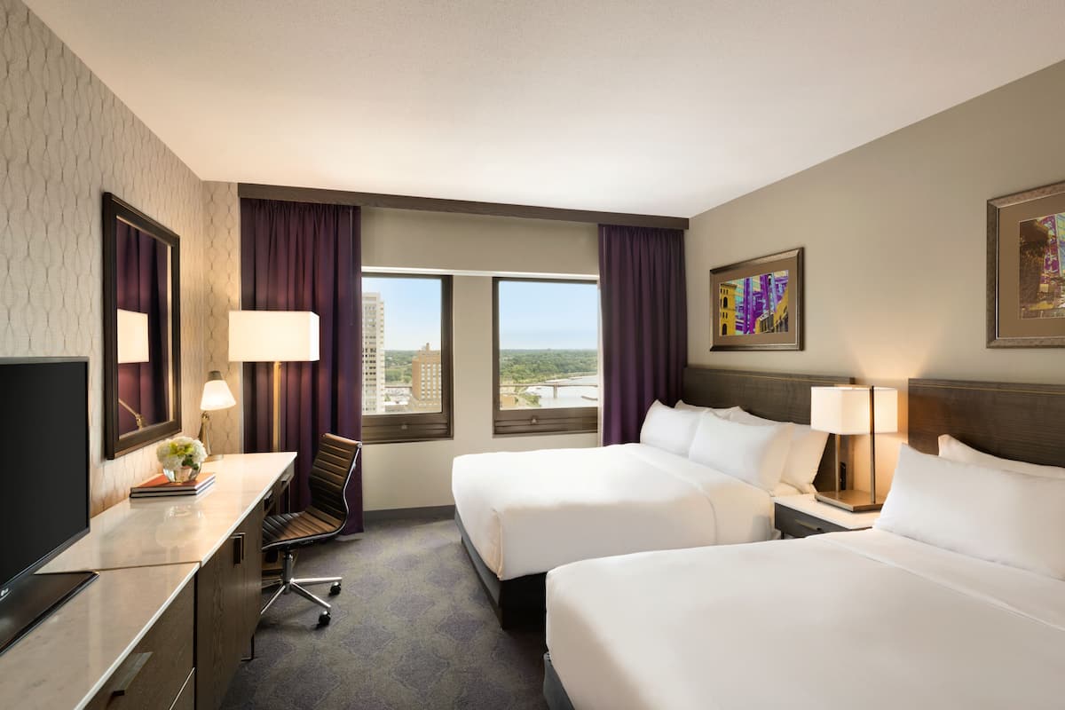 A hotel room with two beds, a desk, a chair, and a TV.