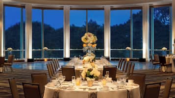 Un comedor formal con una mesa grande dispuesta para una comida, rodeada de sillas y grandes ventanales que ofrecen vistas al exterior.