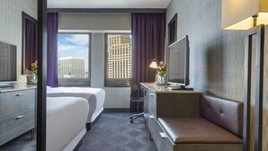 Habitación de hotel con cama, escritorio, computadora, televisor y ventana con cortinas.