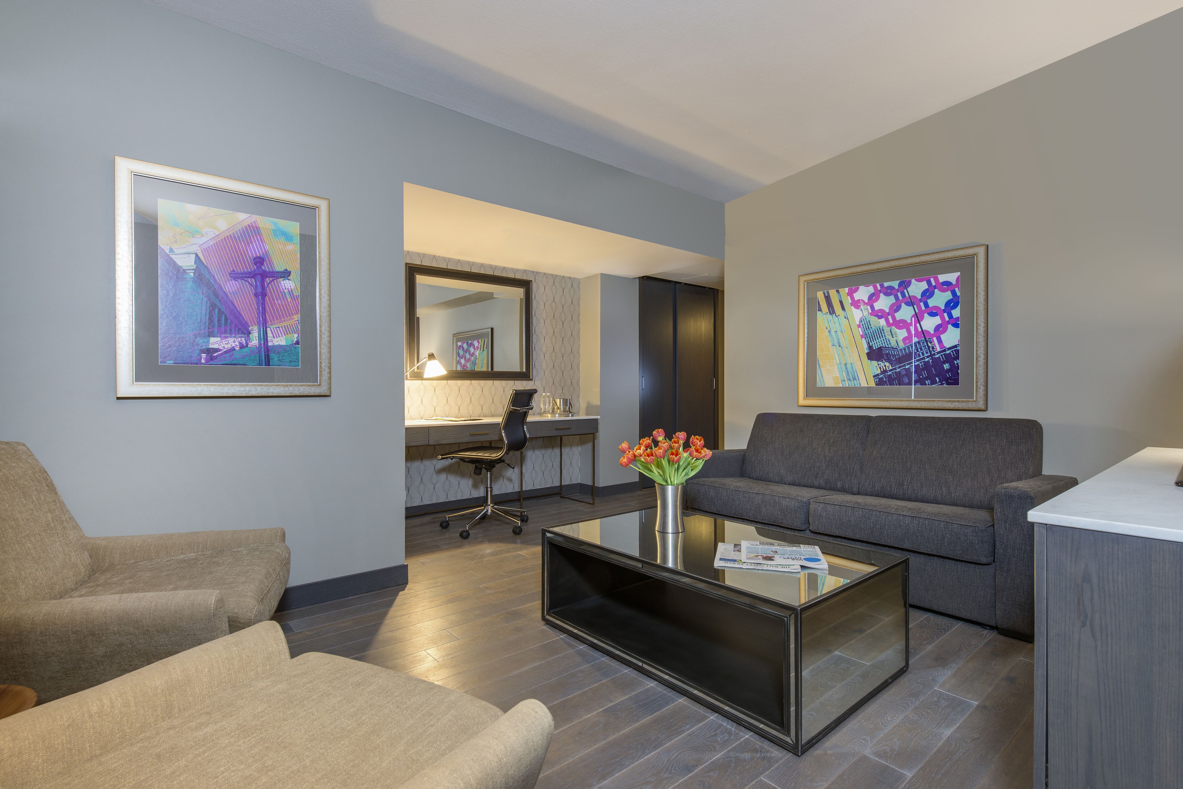 A modern living room with a gray sofa, a glass coffee table, and two framed artworks on the walls.