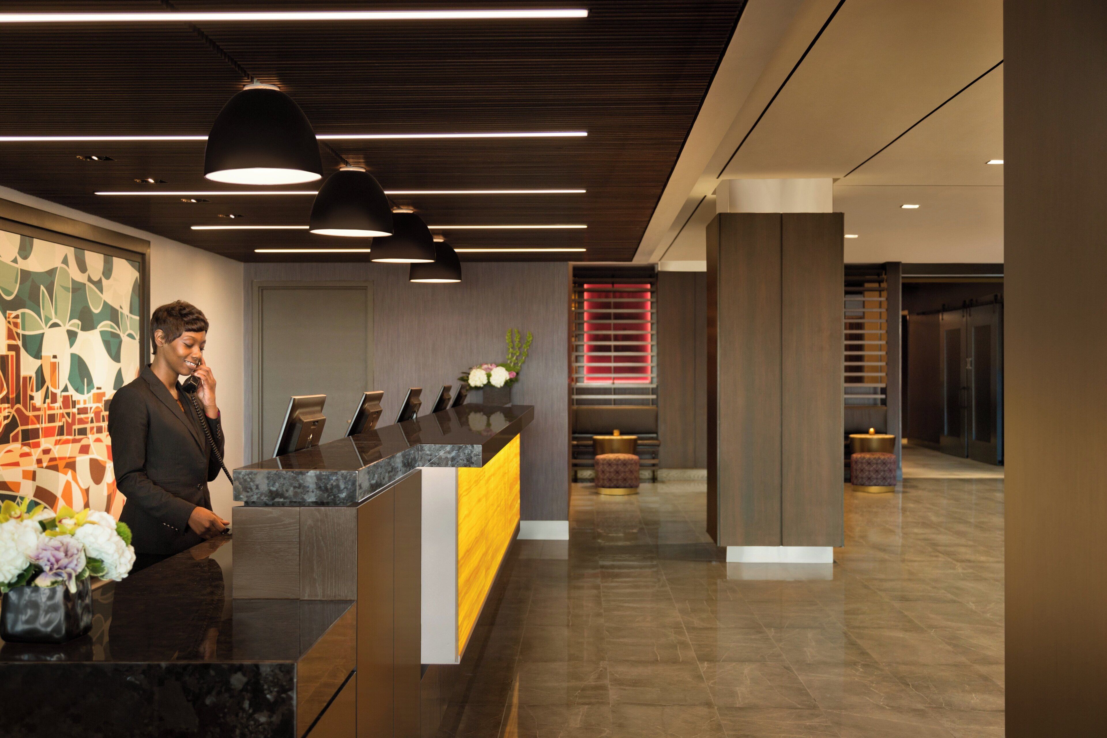 A reception desk with a modern design, featuring a marble top and a wooden accent. There is a vase with flowers on the desk, and a large abstract painting on the wall behind.
