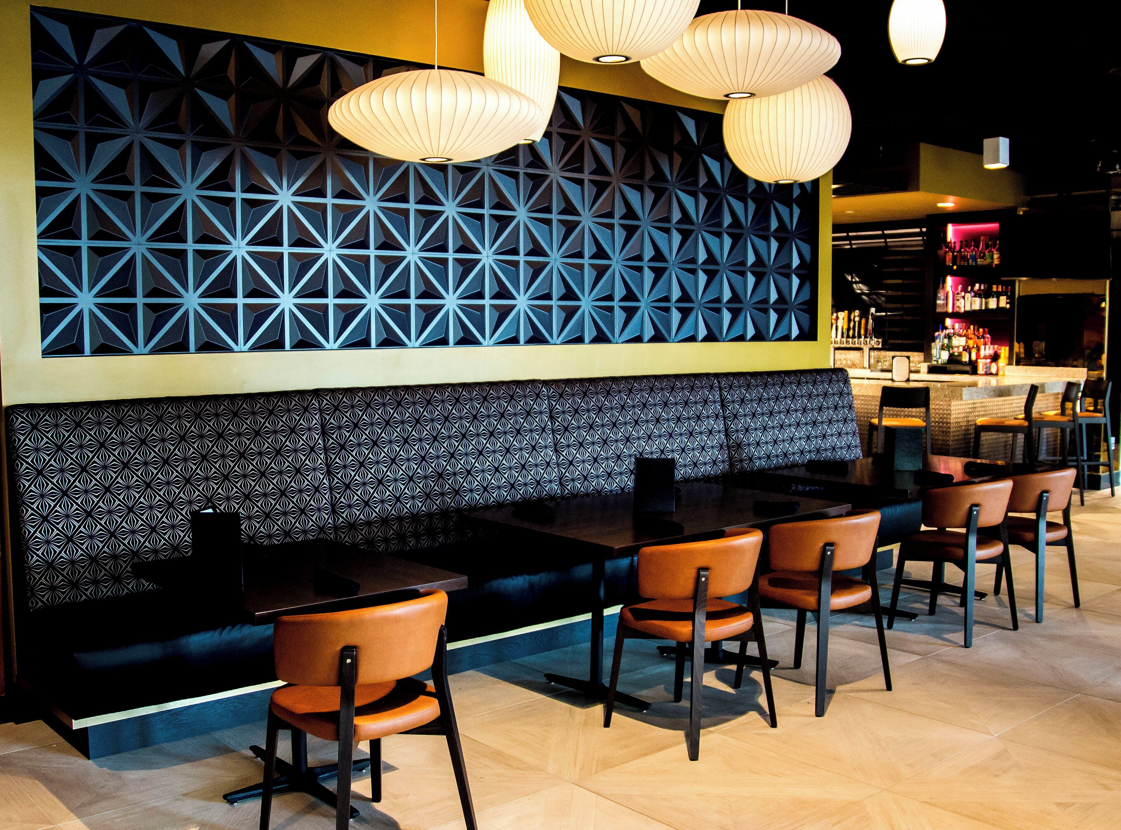 A restaurant interior with a patterned wall, a bar area, and several tables and chairs.