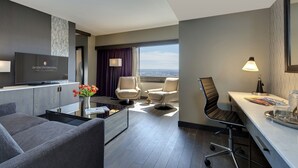 Habitación de hotel moderna con televisión de pantalla plana, asientos cómodos, zona de comedor y vistas a la ciudad.