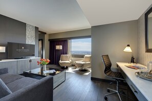 Een moderne hotelkamer met een flatscreen televisie, comfortabele zitplaatsen, een eethoek en uitzicht op de stad.