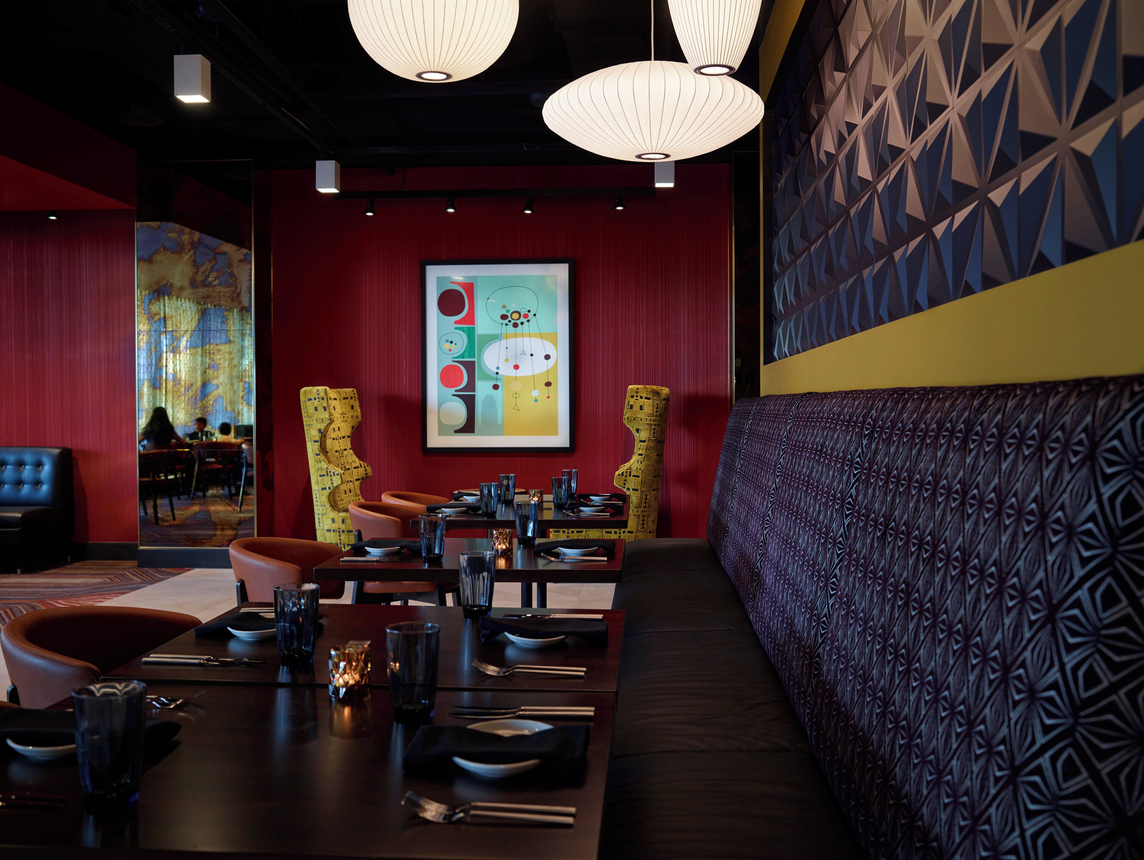 L’intérieur d’un restaurant présente un mur rouge, un grand tableau abstrait et un mur orné de motifs sur le côté droit.