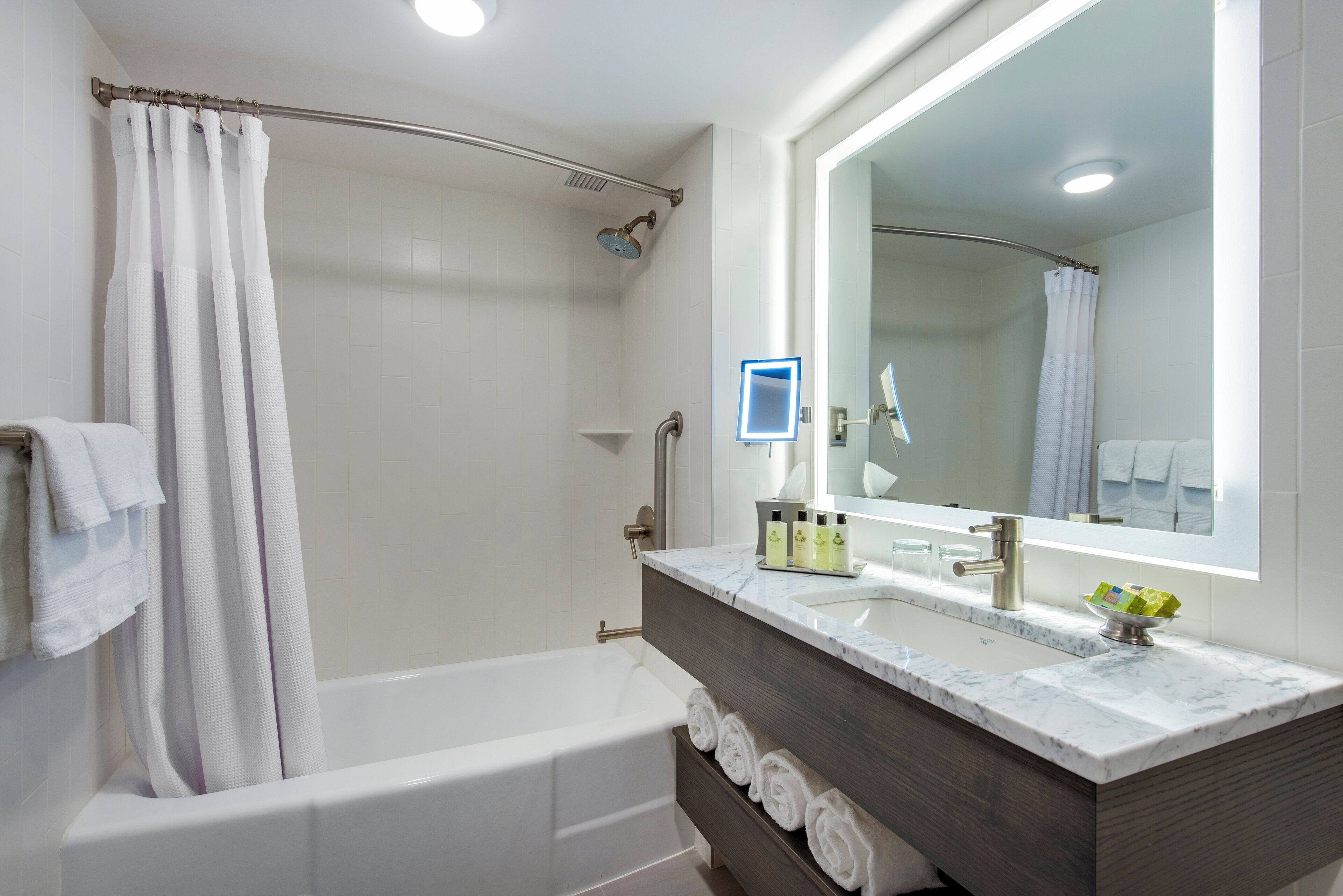 A modern bathroom with a bathtub, shower, vanity with a mirror, and neatly rolled towels.