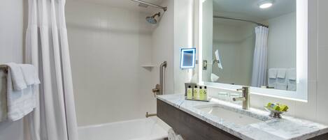 A modern bathroom with a bathtub, shower, vanity with a mirror, and neatly rolled towels.
