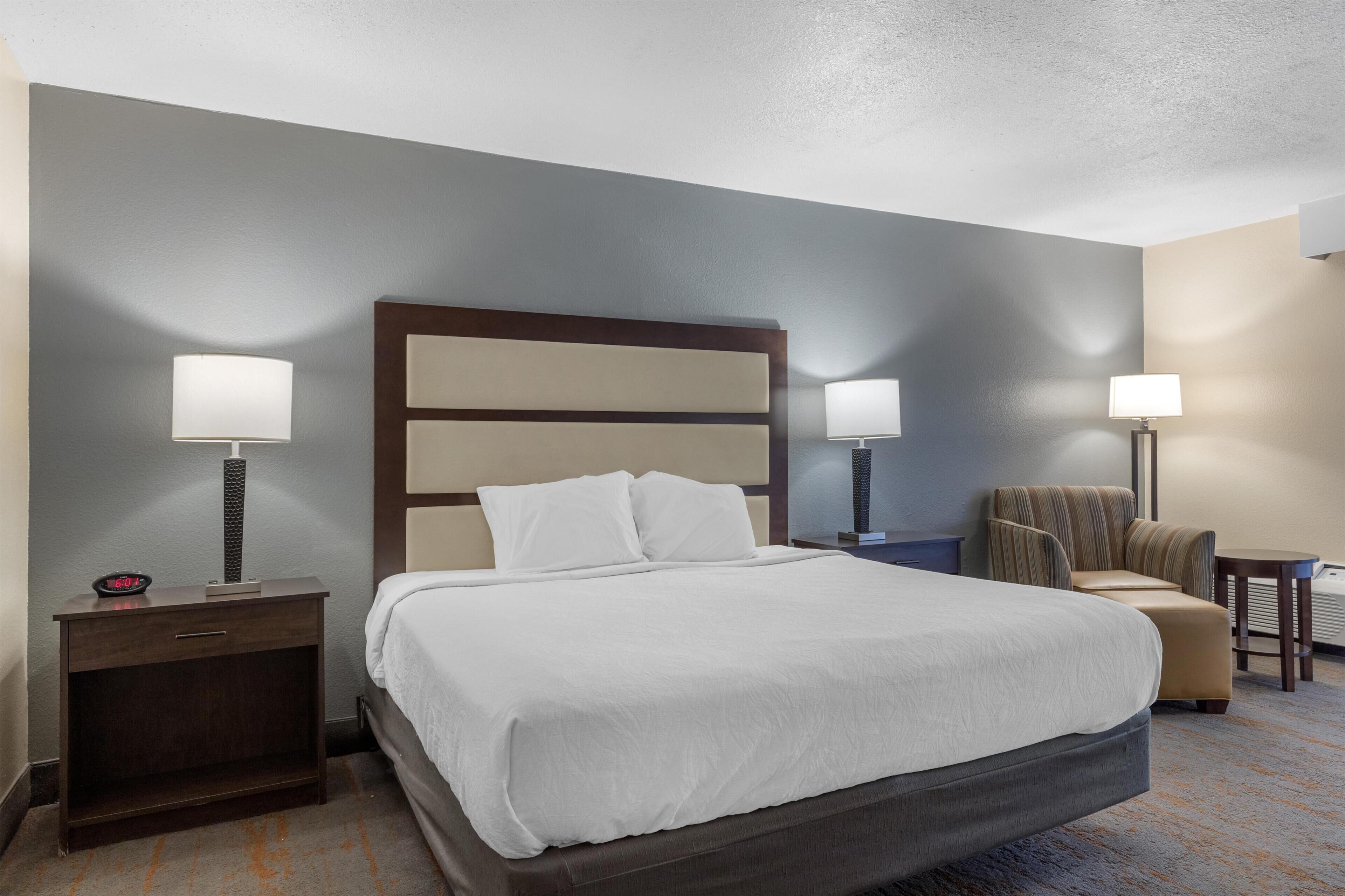 A hotel room with a large bed, two bedside tables with lamps, a chair, and a small table.