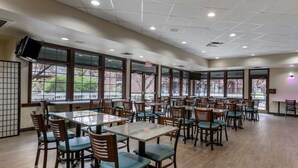 A spacious dining area with multiple tables and chairs, large windows with a view, and a flat-screen TV mounted on the wall. - Best Western Sunridge Inn & Conference Center (Baker City)