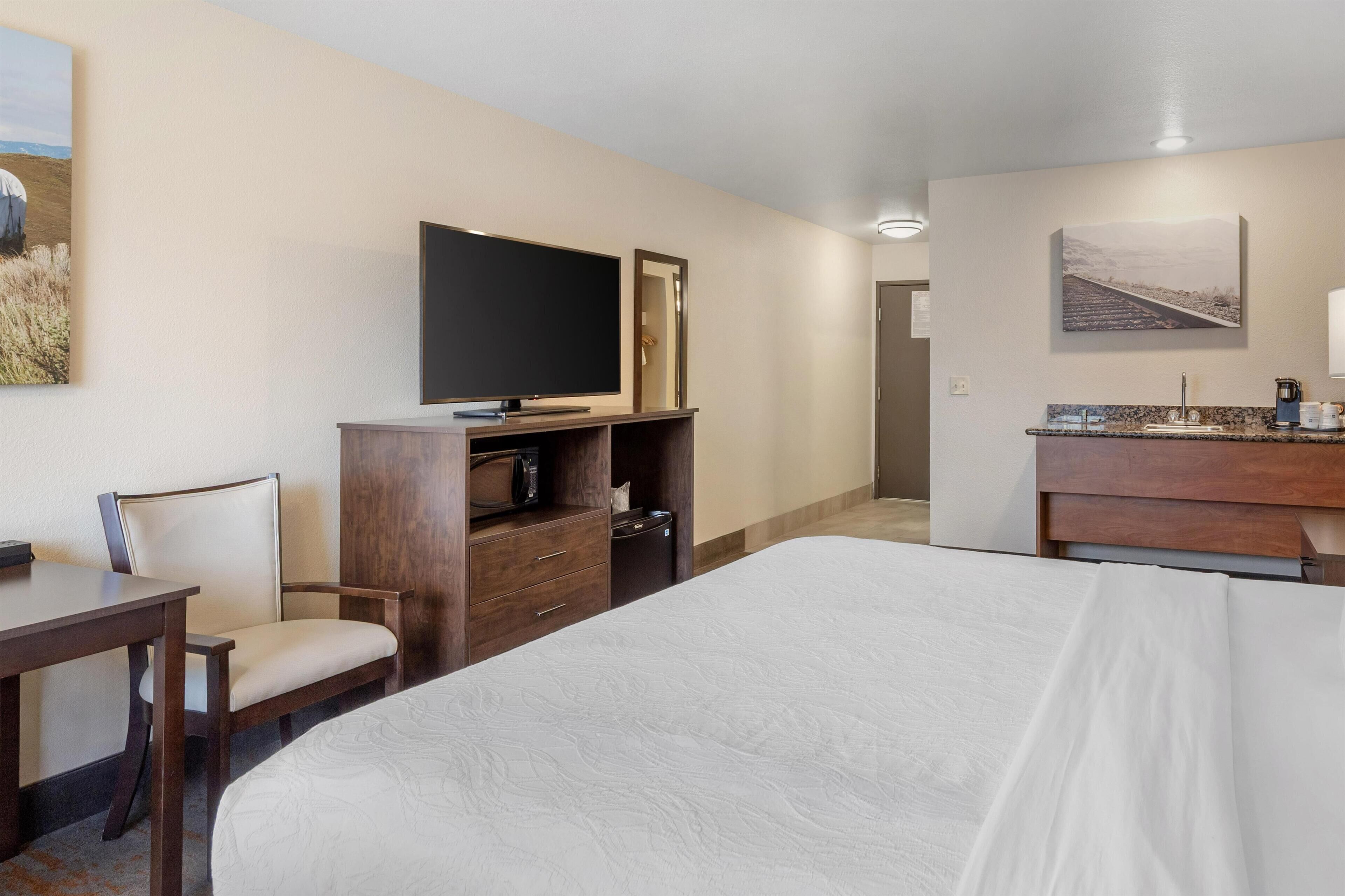 Una camera d'albergo con un letto, una televisione, una scrivania, una sedia, un comò e un quadro appeso al muro.