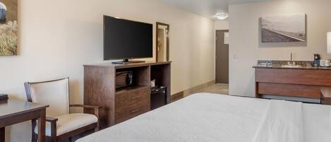 Una camera d'albergo con un letto, una televisione, una scrivania, una sedia, un comò e un quadro appeso al muro.