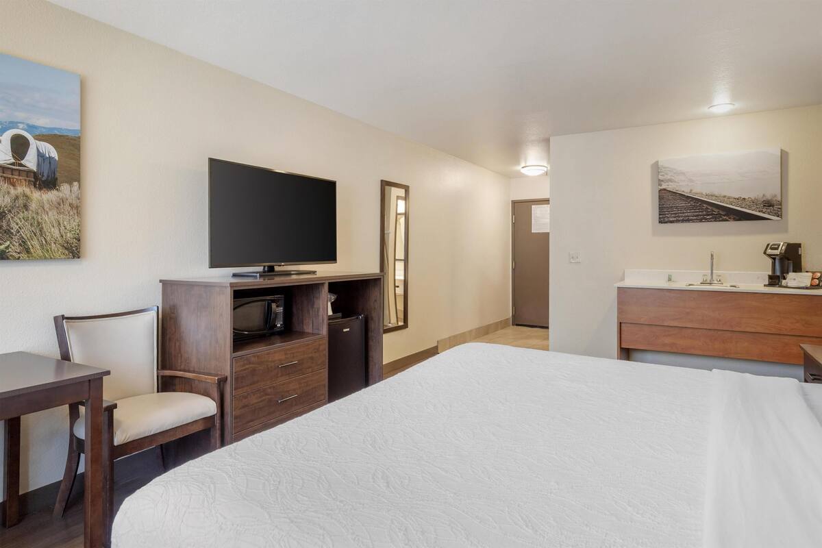 Une chambre d’hôtel avec un grand lit, une télévision, un bureau, une chaise, une commode et un miroir.