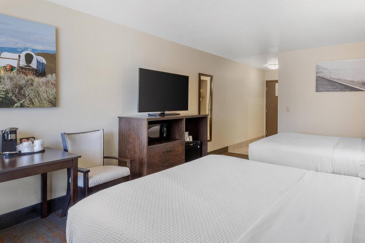 A hotel room with two beds, a TV, a desk with a chair, and a coffee maker.
