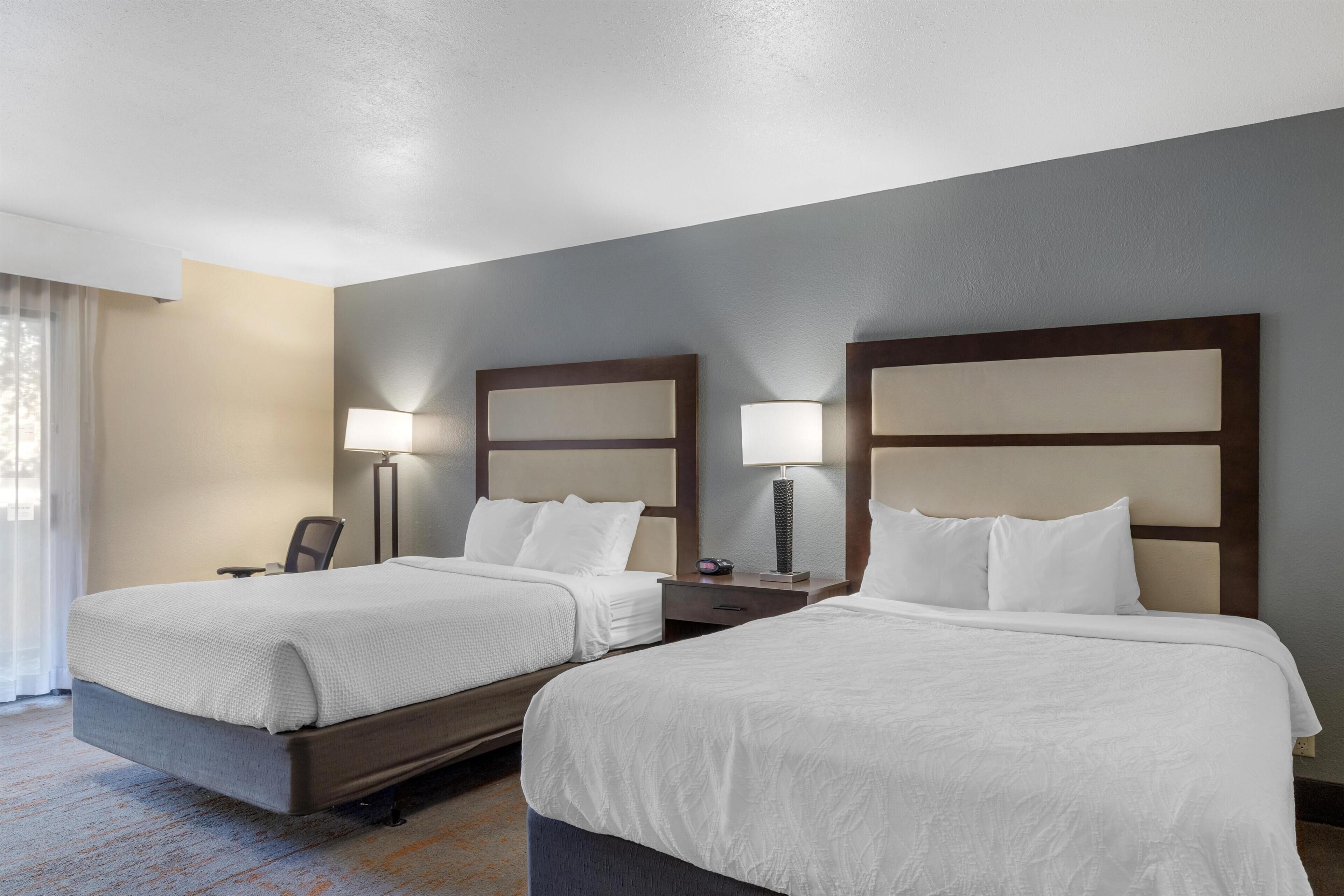 Une chambre d’hôtel avec deux lits, un bureau, une chaise et deux lampes de chevet.