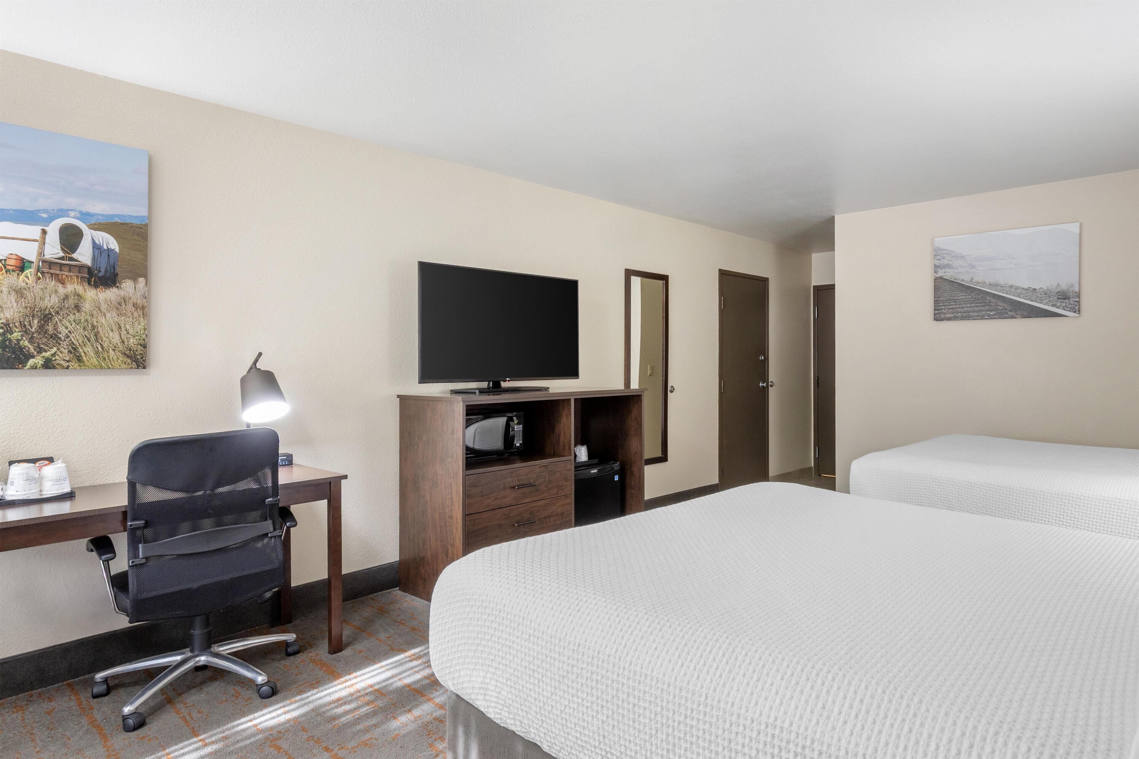 A hotel room with a desk, office chair, television, two beds, and artwork on the walls.