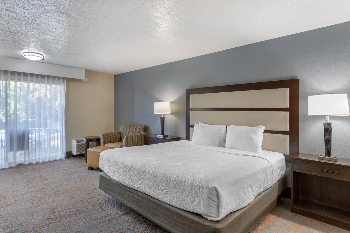 A hotel room with a large bed, a desk, a chair, a lamp, and a window with curtains.