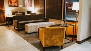 A modern living room with a sofa, ottoman, armchair, and a glass coffee table. There are two side tables with lamps, a large window, and artwork on the wall. - Best Western Sunridge Inn & Conference Center (Baker City)