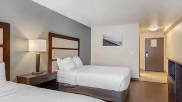 A hotel room with two beds, a nightstand, a lamp, a picture on the wall, and a door leading to a hallway.
