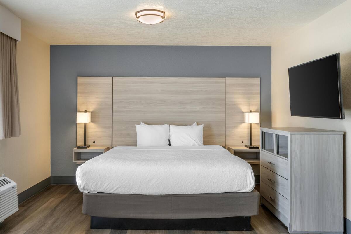 A hotel room with a large bed, bedside lamps, a flat-screen TV, and a dresser.