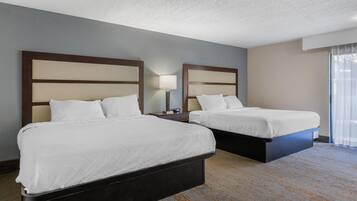 Habitación de hotel con dos camas, una mesita de noche, una lámpara y un ventanal con cortinas.