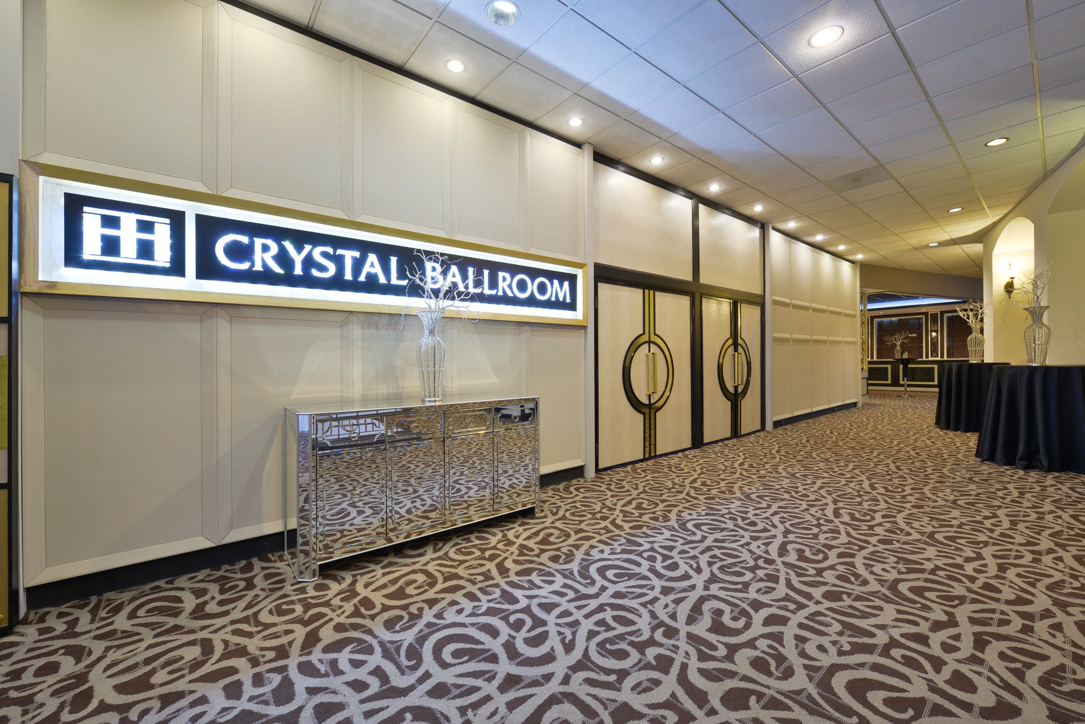 Un pasillo de hotel con un letrero que dice "Crystal Ballroom", un piso con estampado y una zona de recepción con una vitrina de cristal.