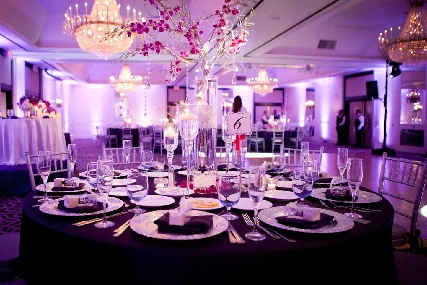 Une salle de banquet avec des tables rondes dressées pour un événement formel, agrémentée de décorations de table élégantes et de compositions florales.