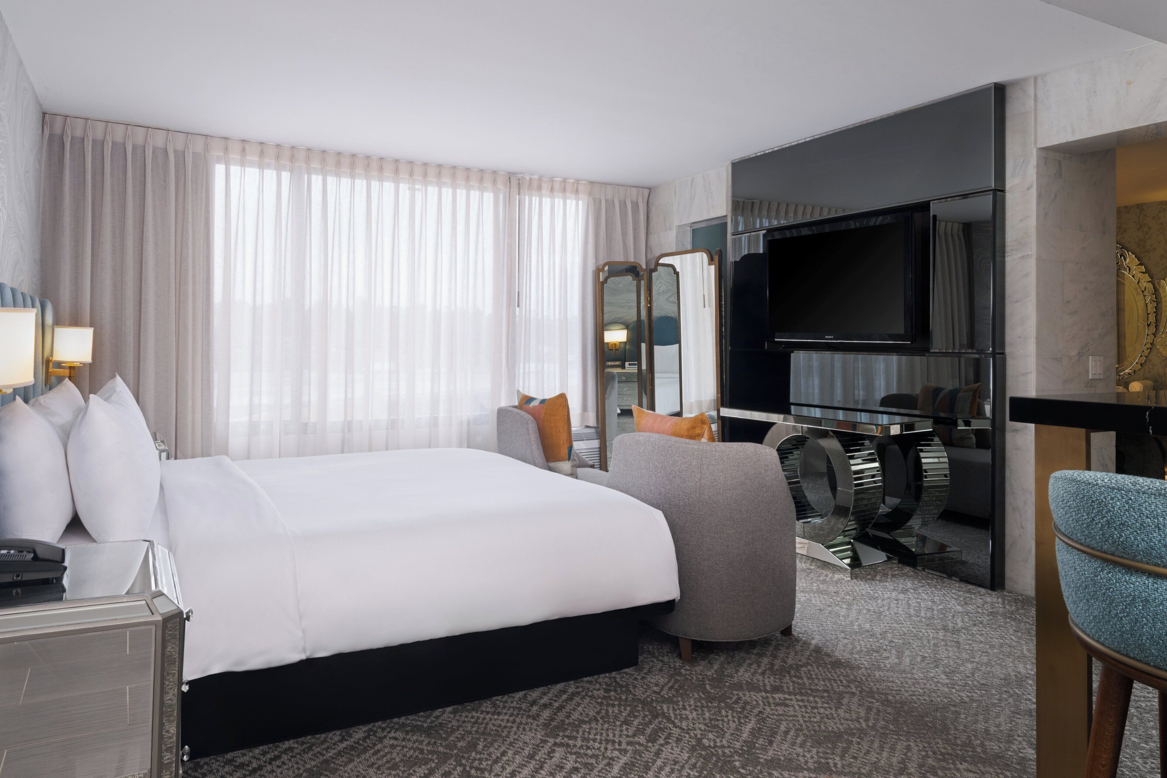 A hotel room with a large bed, a desk with a computer, a television, and a seating area with a chair and a sofa.