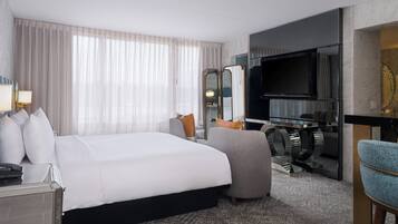 A hotel room with a large bed, a desk with a computer, a television, and a seating area with a chair and a sofa.