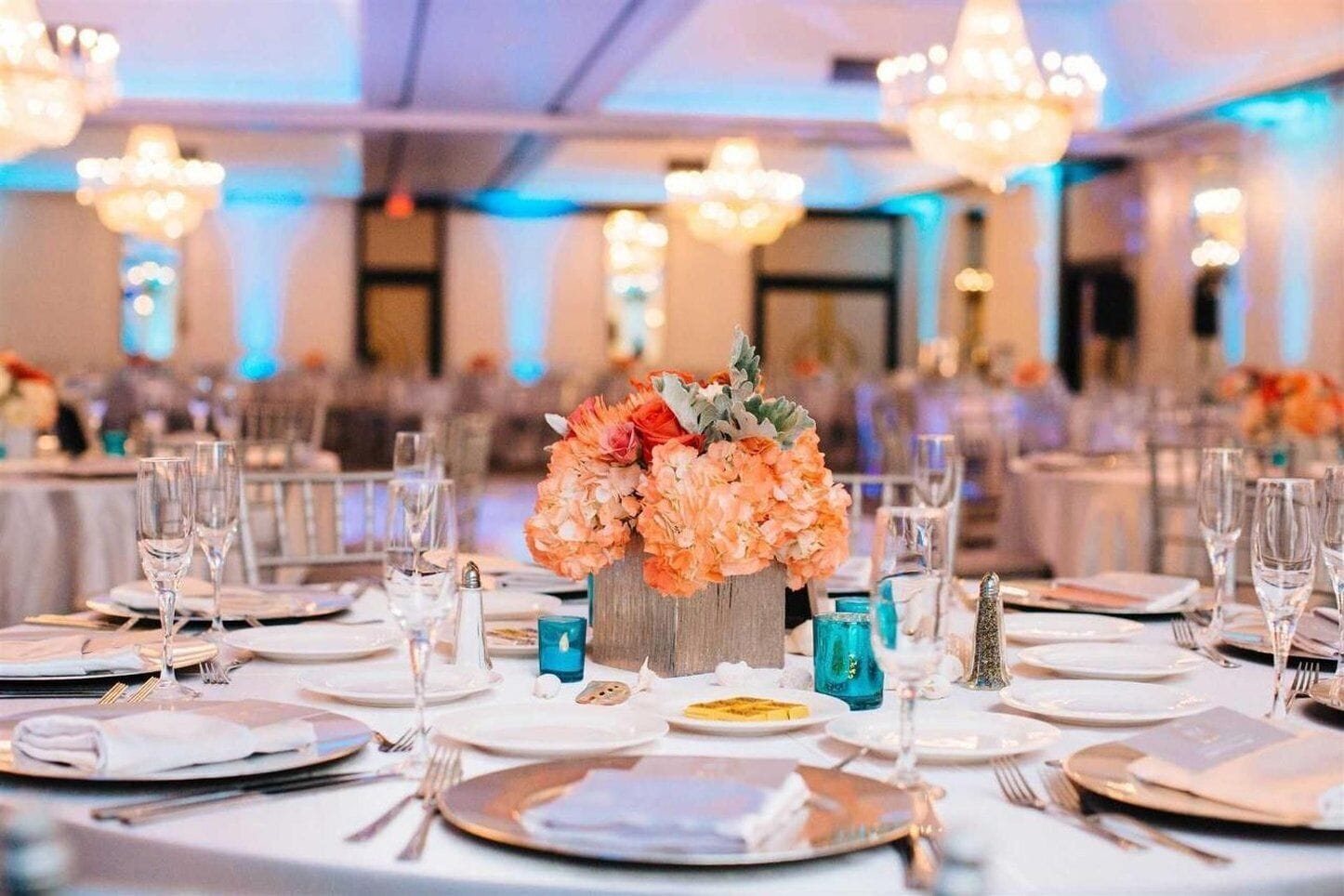 A banquet hall with round tables set for a formal event, featuring floral centerpieces and blue candle holders.