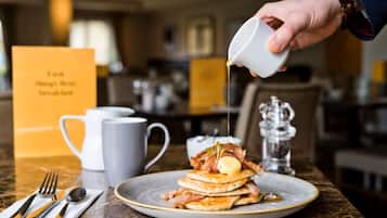 Un desayuno con tortitas cubiertas de tocino y mantequilla, una taza de café y una tarjeta de menú.