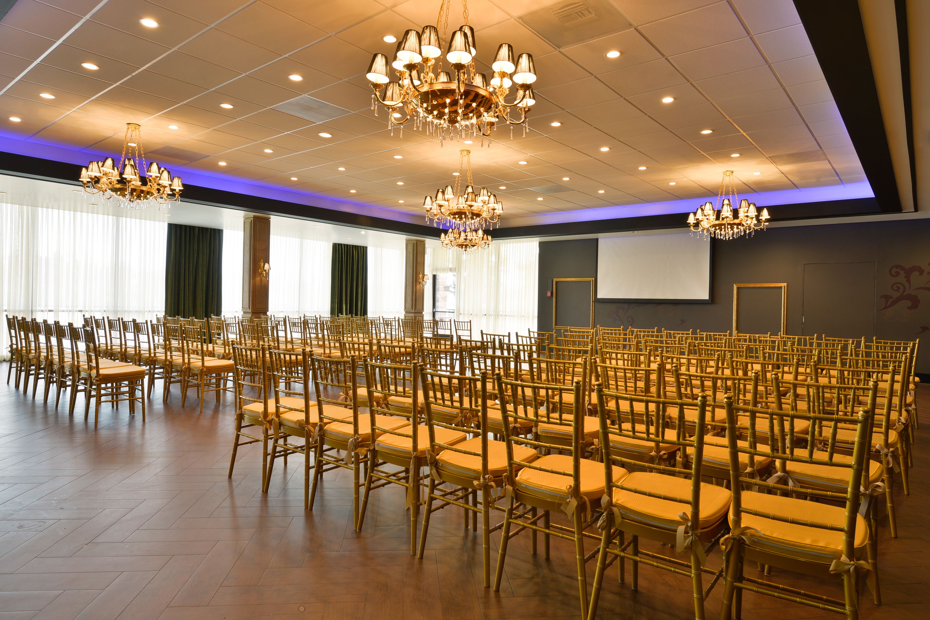 A conference room with rows of chairs, chandeliers, and a large screen.