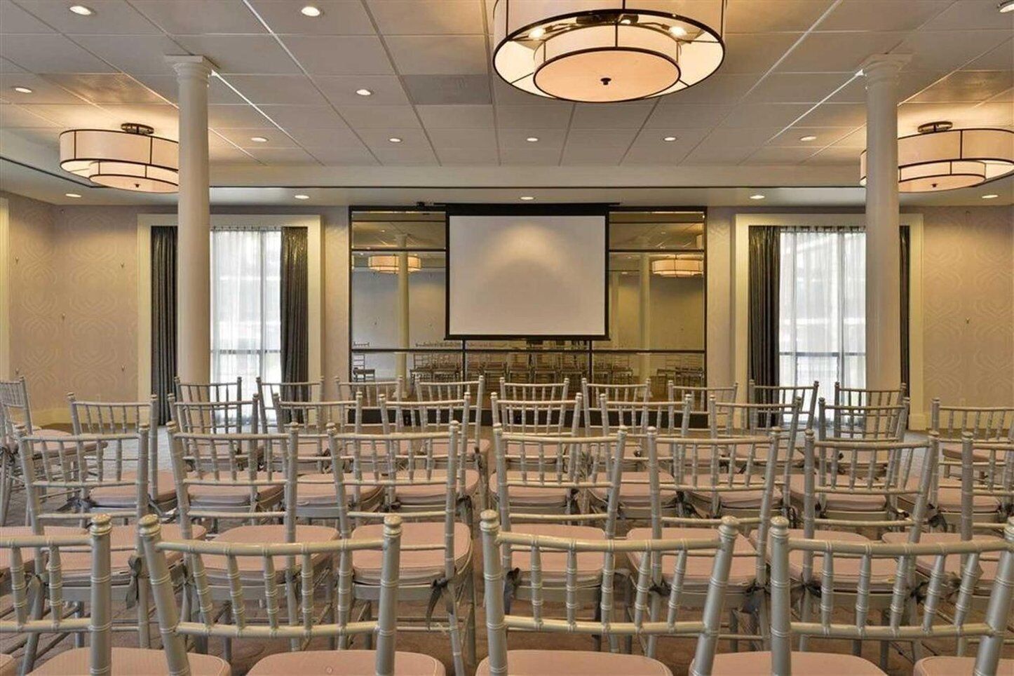 A conference room with rows of chairs, a large screen, and a chandelier.