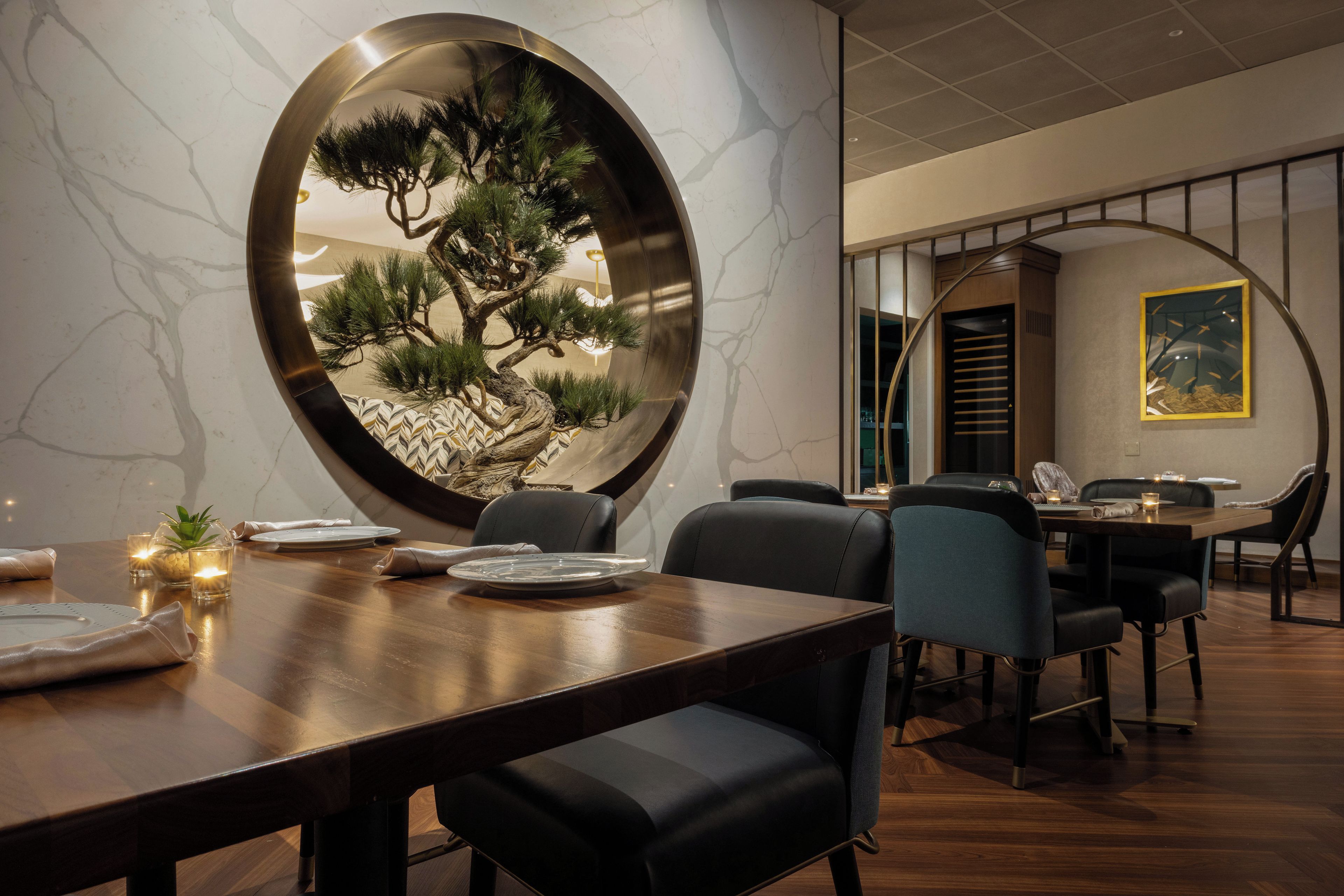 Un comedor con un espejo redondo que refleja un pino, una mesa de madera y sillas.
