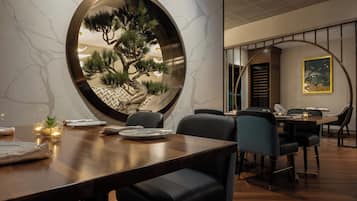 Un comedor con un espejo redondo que refleja un pino, una mesa de madera y sillas.