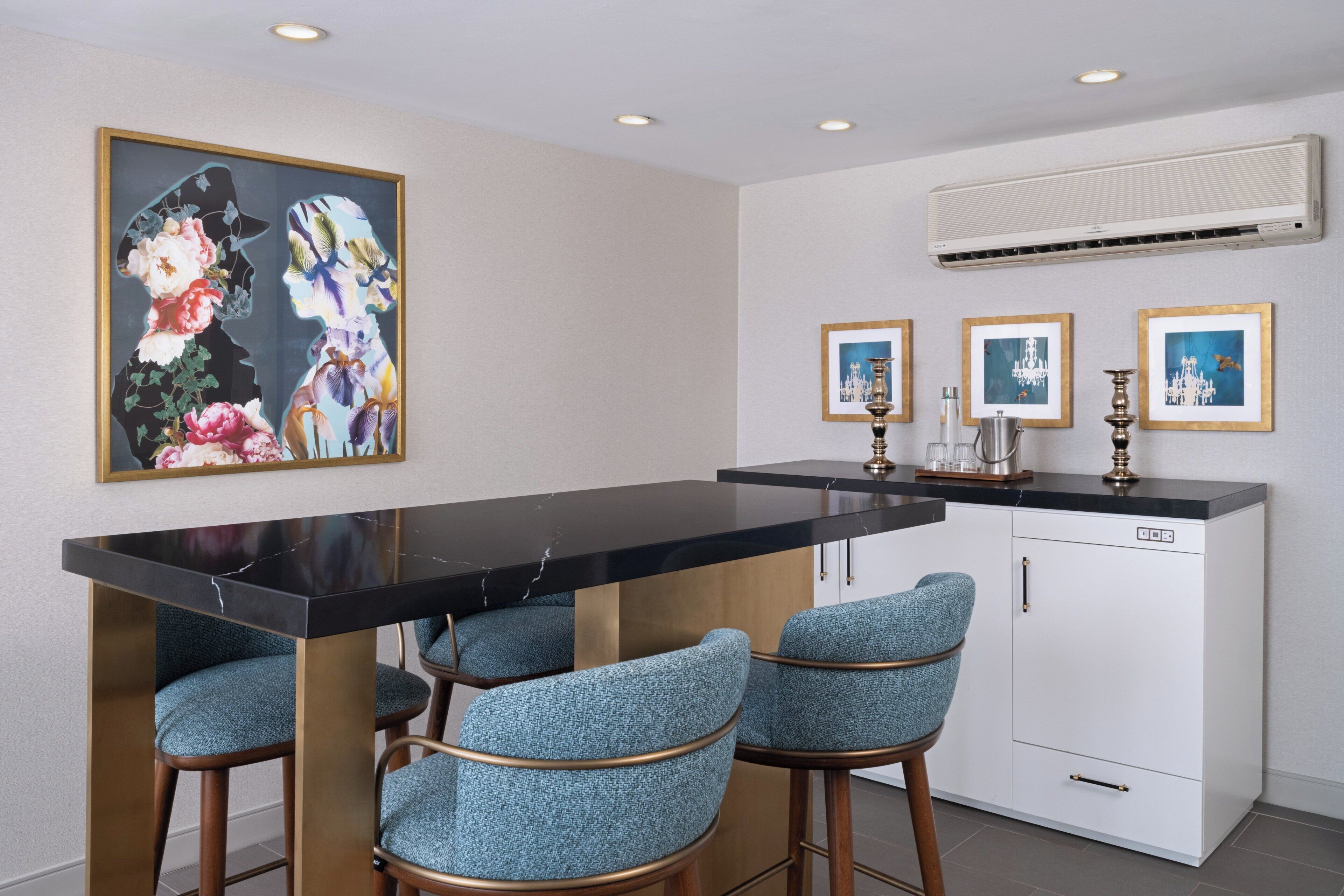 A modern kitchen with a black marble countertop, bar stools, and a large framed floral artwork.