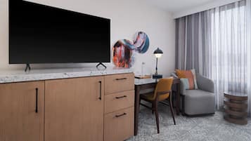 A modern hotel room with a large flat-screen TV, a desk with a chair, a sofa, and a decorative lamp.