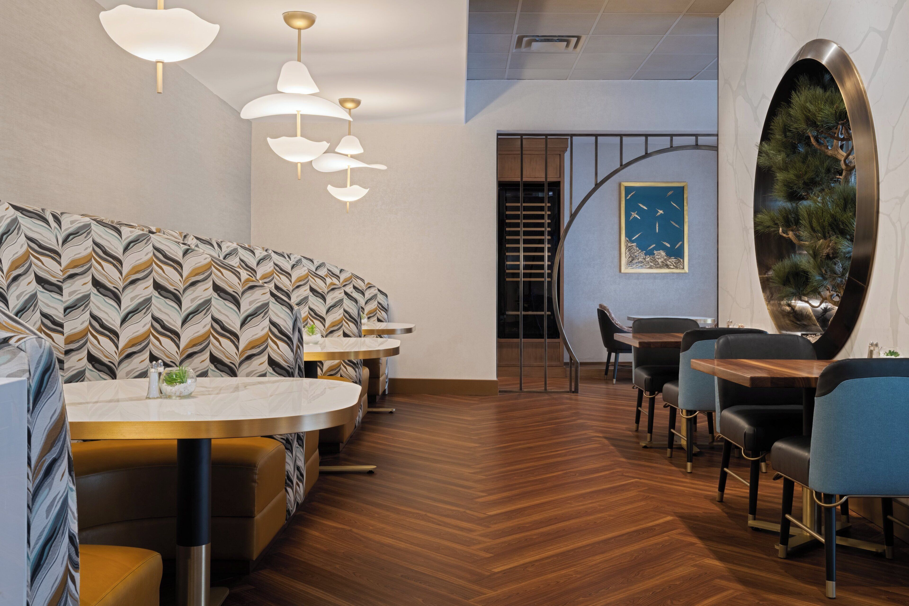 A modern restaurant interior with a patterned sofa, round tables, and a unique wall art piece.