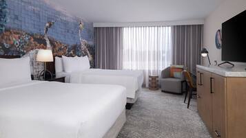 A hotel room with two beds, a desk, a chair, a TV, and a large window with curtains.