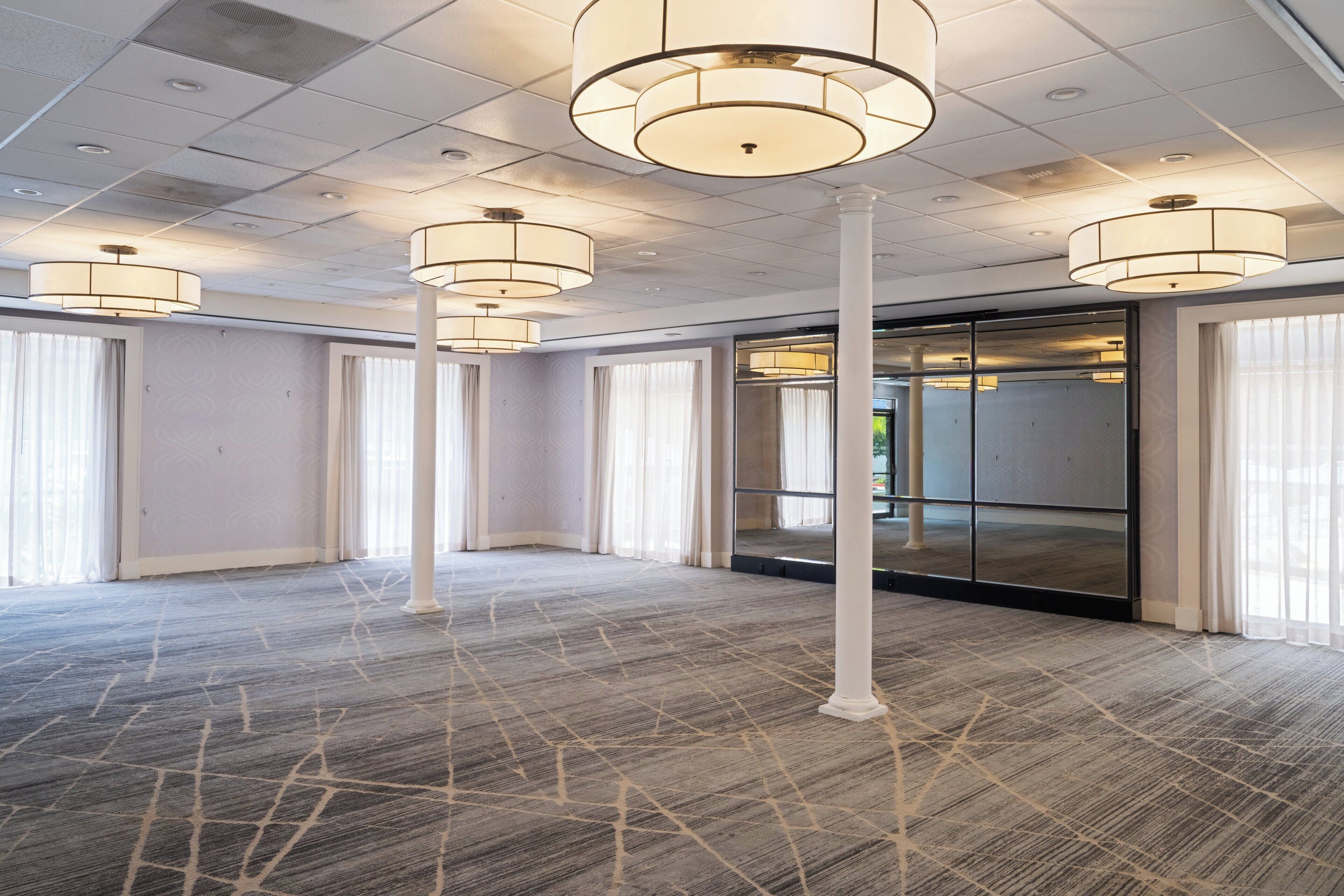 A spacious room with a patterned carpet, large windows with curtains, and multiple ceiling lights.
