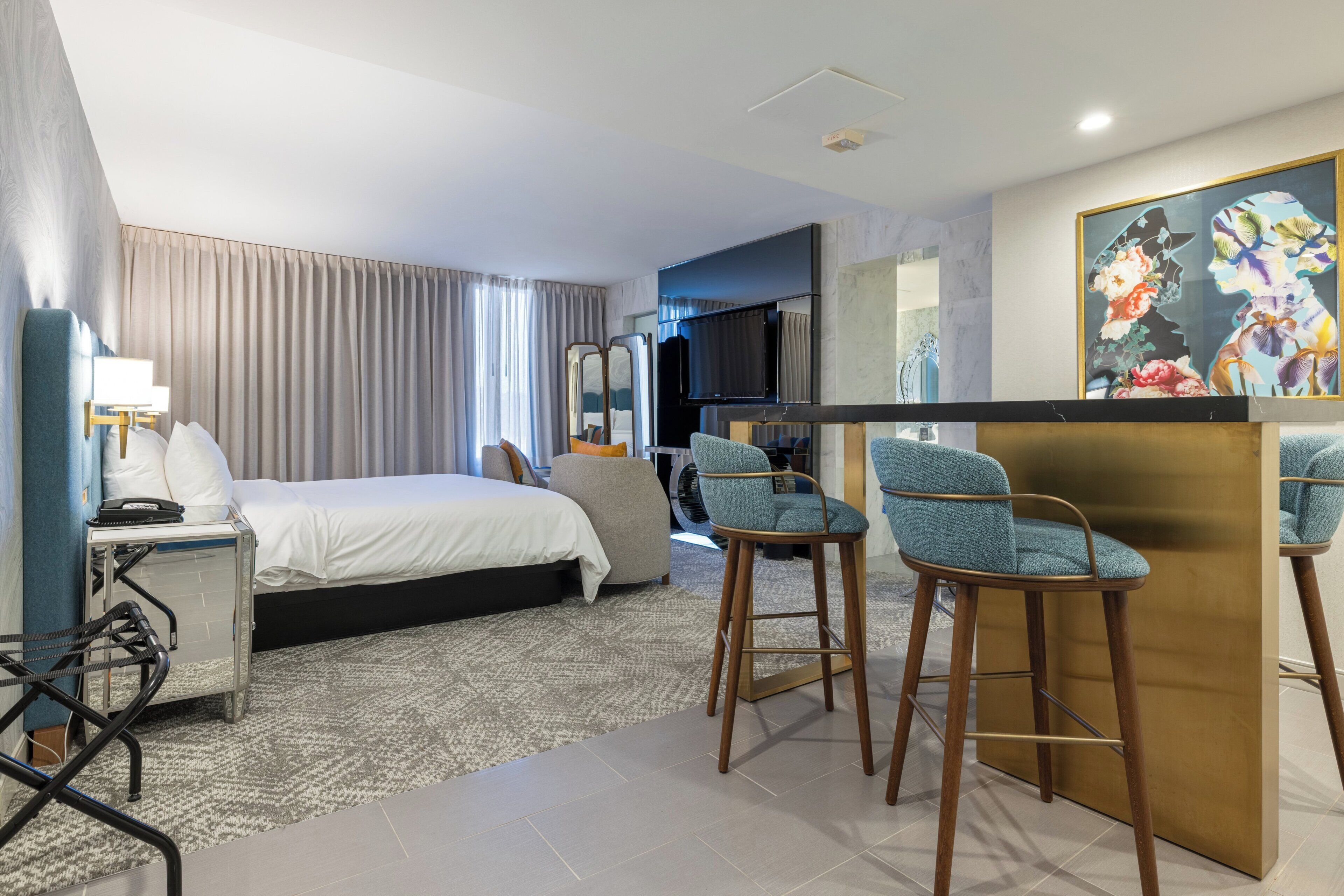 Hotelkamer met een bed, een bureau met lamp, twee barkrukken, een televisie en een schilderij aan de muur.