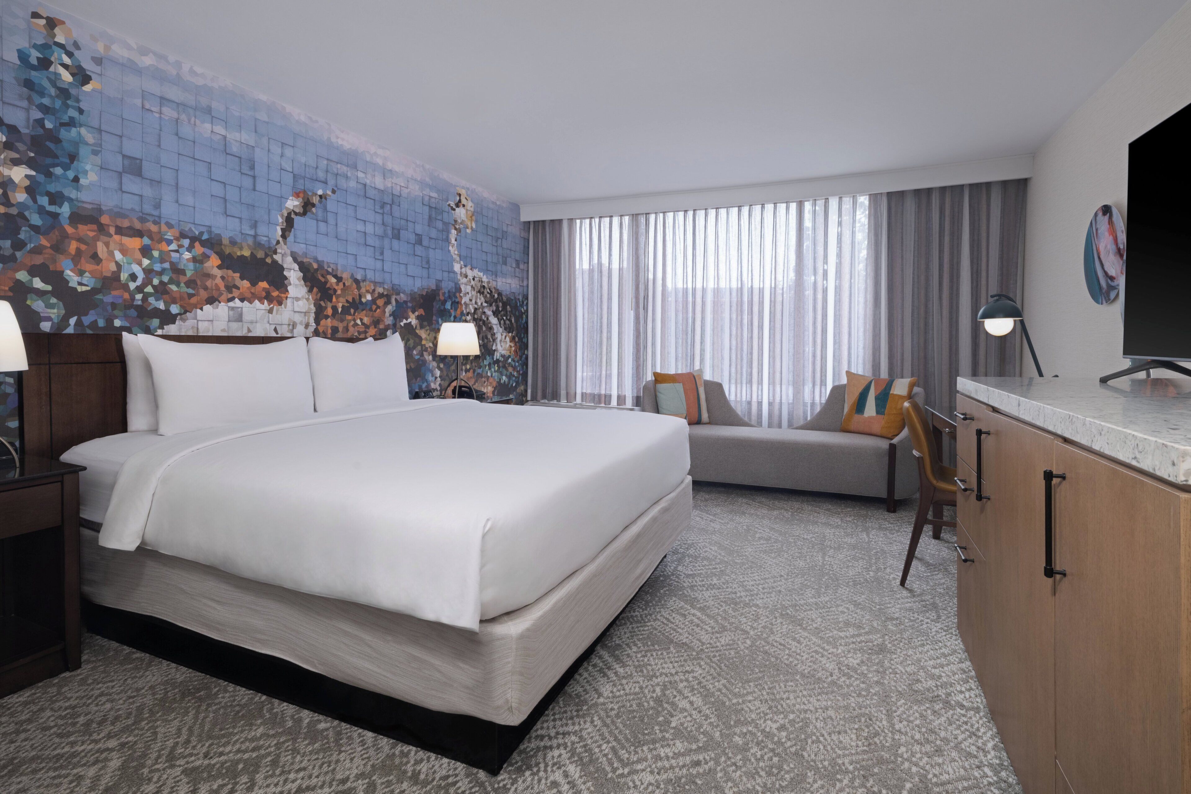 A hotel room with a large bed, a sofa, a desk, and a television.