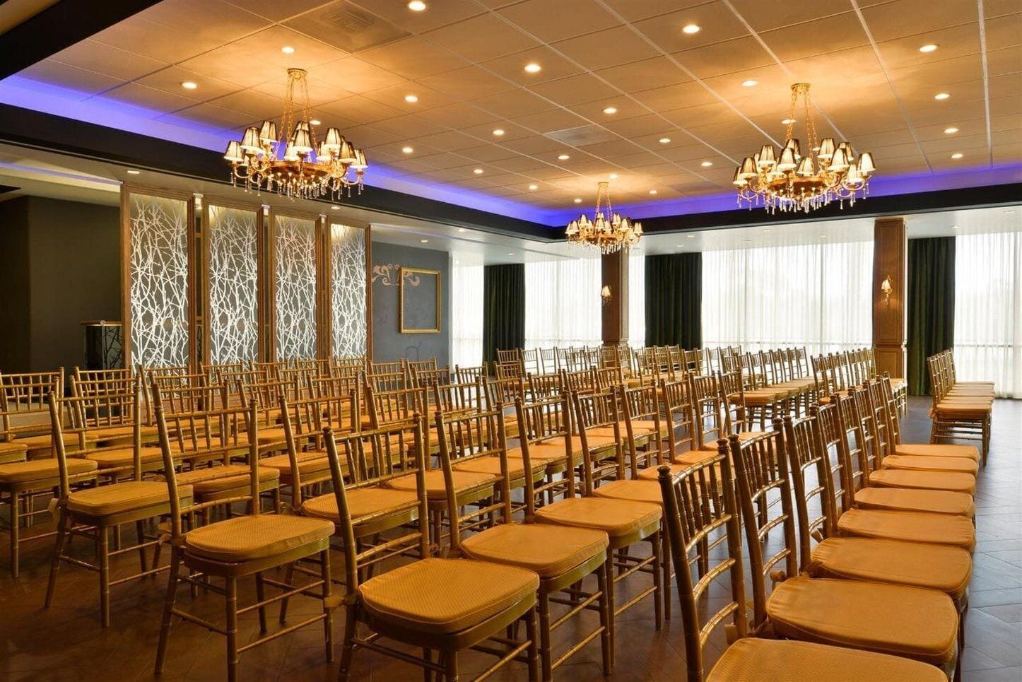 Un salón de conferencias con filas de sillas y mesas de madera, candelabros y un papel tapiz decorado.