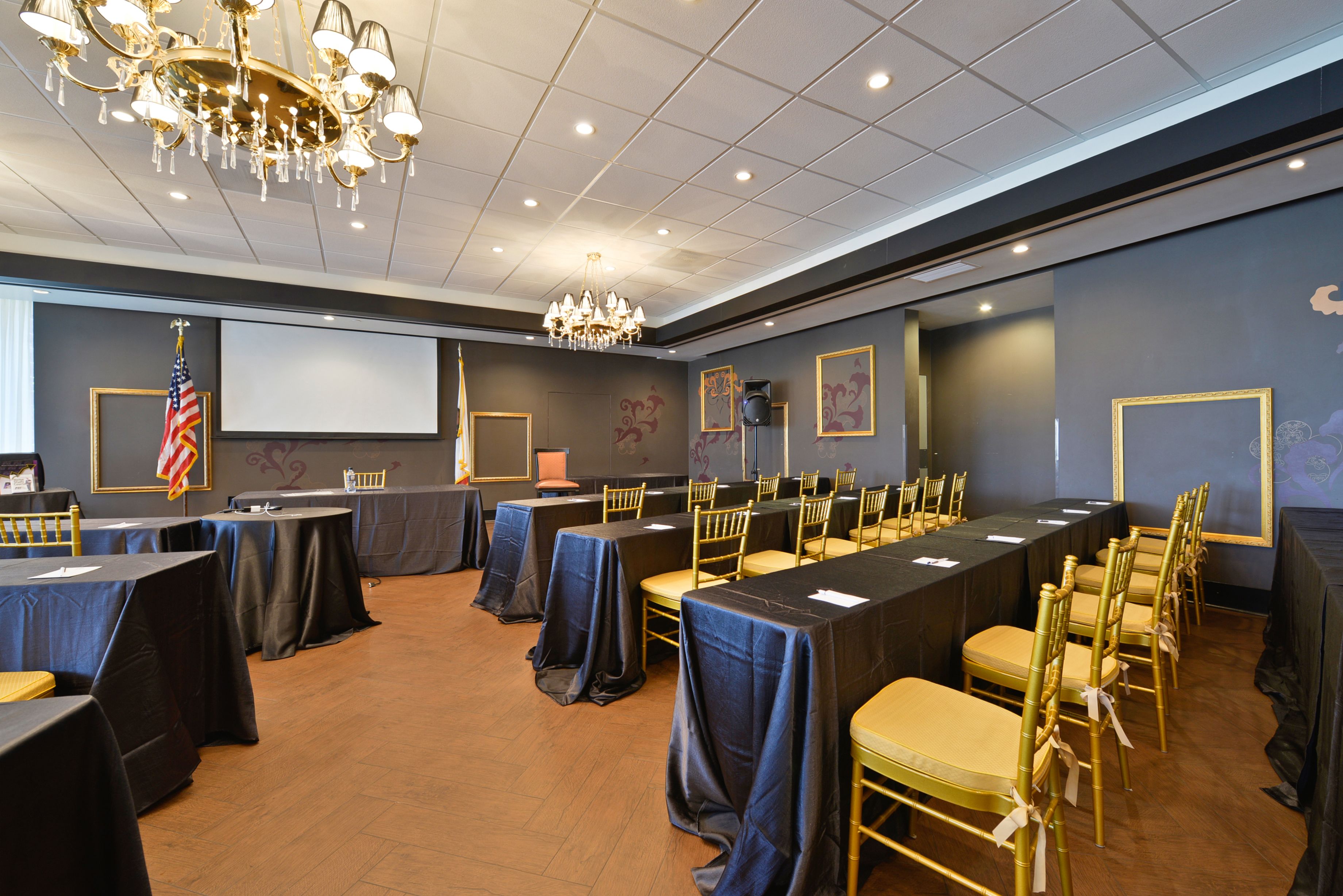 A conference room with tables and chairs, a projector screen, and an American flag.