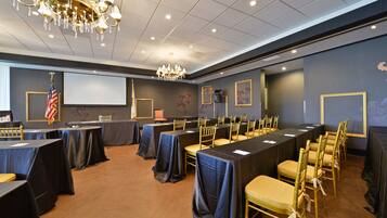 A conference room with tables and chairs, a projector screen, and an American flag.