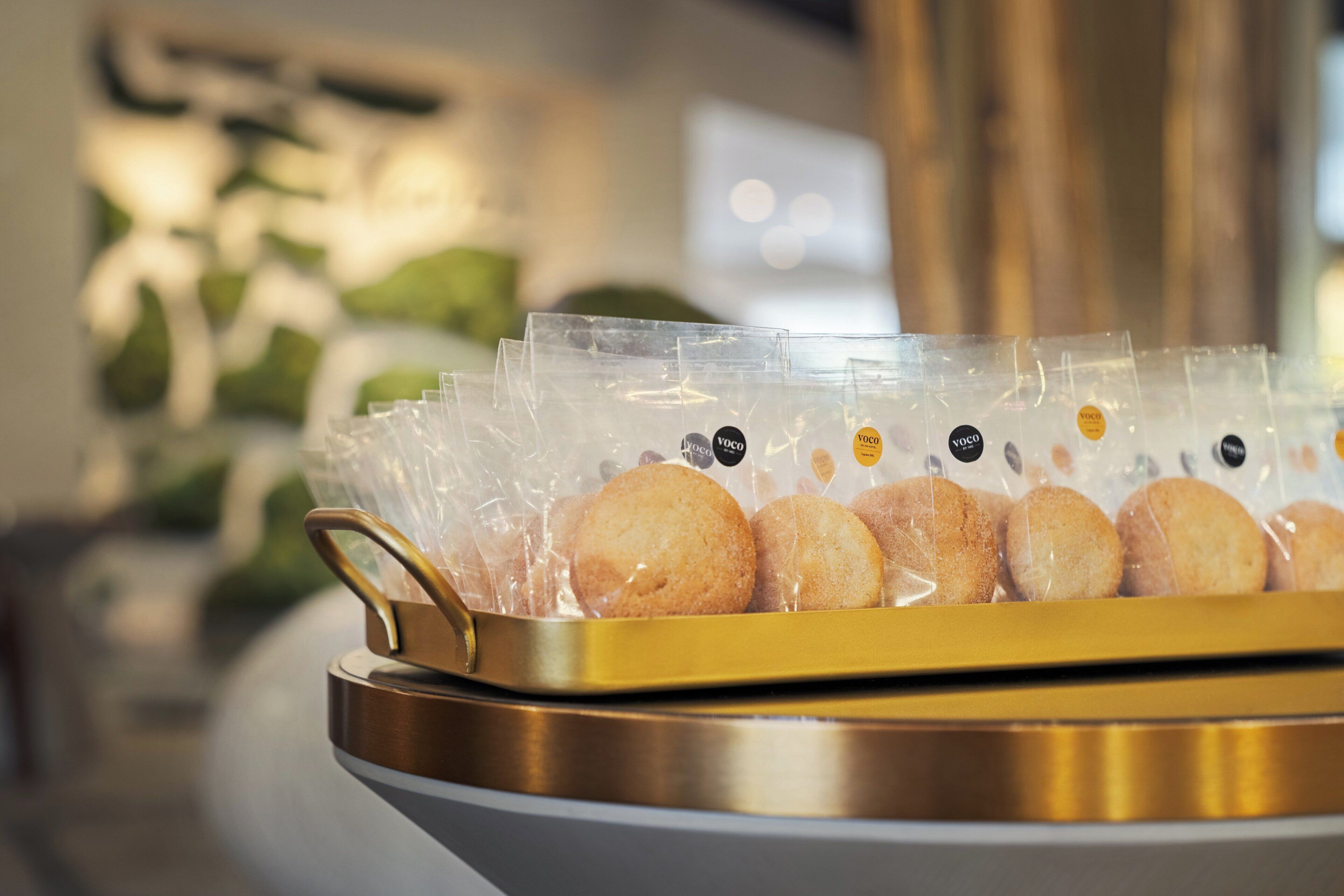 Una bandeja de pasteles redondos y azucarados en un recipiente de plástico transparente con un asa dorada.
