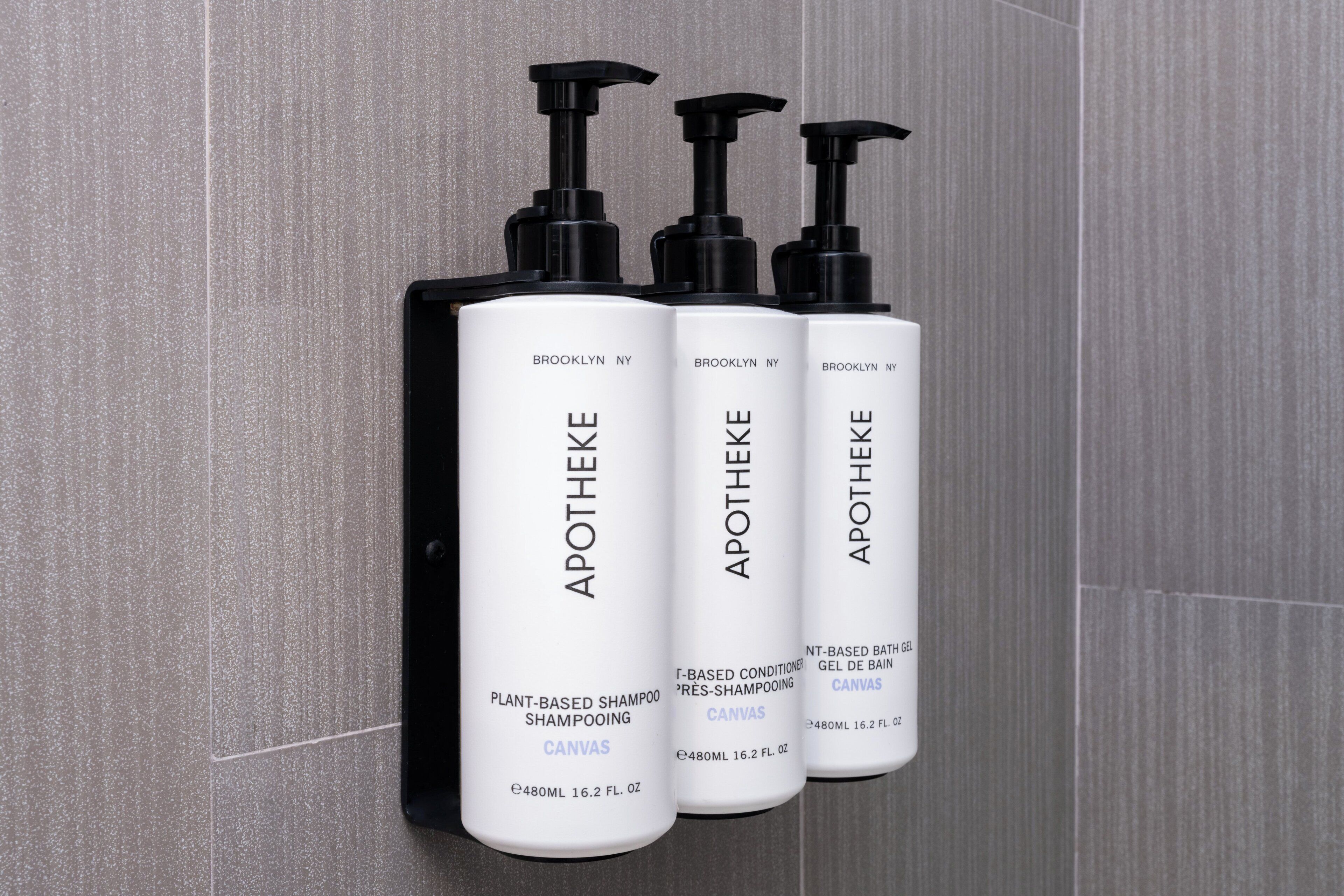 Three bottles of Apotheke plant-based shampoo on a tiled wall.